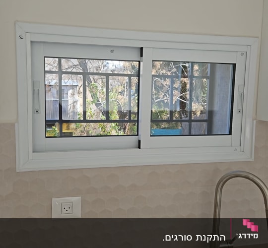 חלון עם מסגרת לבנה ומסגרת פנימית שחורה